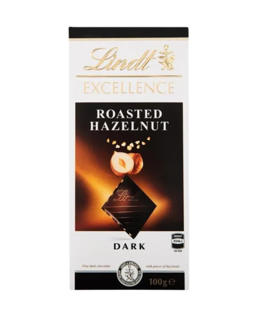 Lindt Excellence Roasted Hazelnut Dark Chocolate bar, 100g. Elegant packaging featuring a black and white design with gold accents. Showcases roasted hazelnuts and dark chocolate pieces, perfect for chocolate lovers.